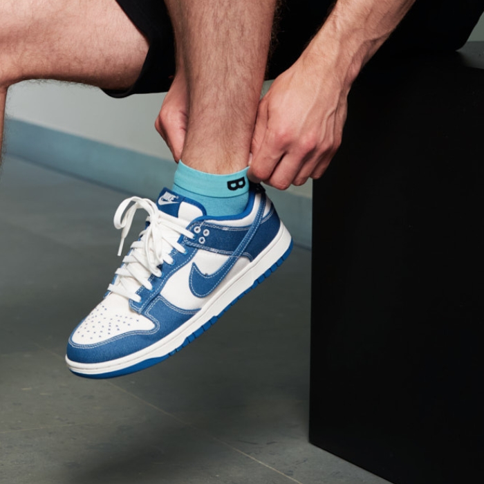 Laurens de Vries trekt zijn effen blauwe Plug & Play sokken perfect aan, zichtbaar boven zijn blauwe Nike Dunk Low sneakers.